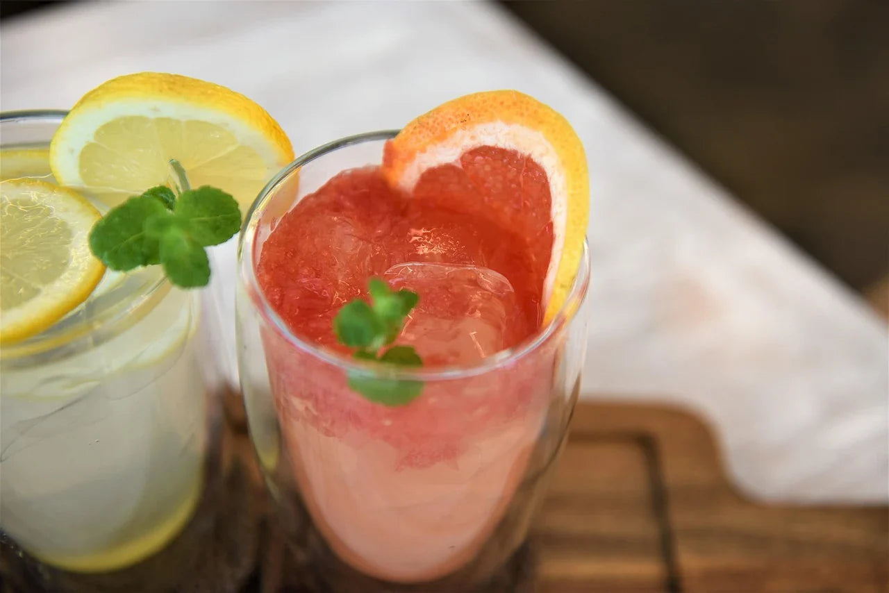 Two refreshing drinks on a tray: one grapefruit juice with a slice and mint, and one lemon water with lemon slice and mint. Bright and inviting.