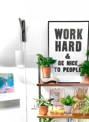 Shelves with potted plants and decor beneath a motivational poster stating, "Work Hard & Be Nice to People. White Soltech Aspected mounted with a black wall mount on the wall