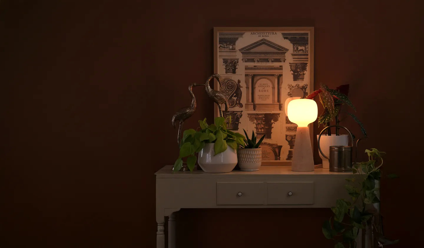 Dimly lit room with a table holding decorative items including a lamp, plants, and a framed picture.
