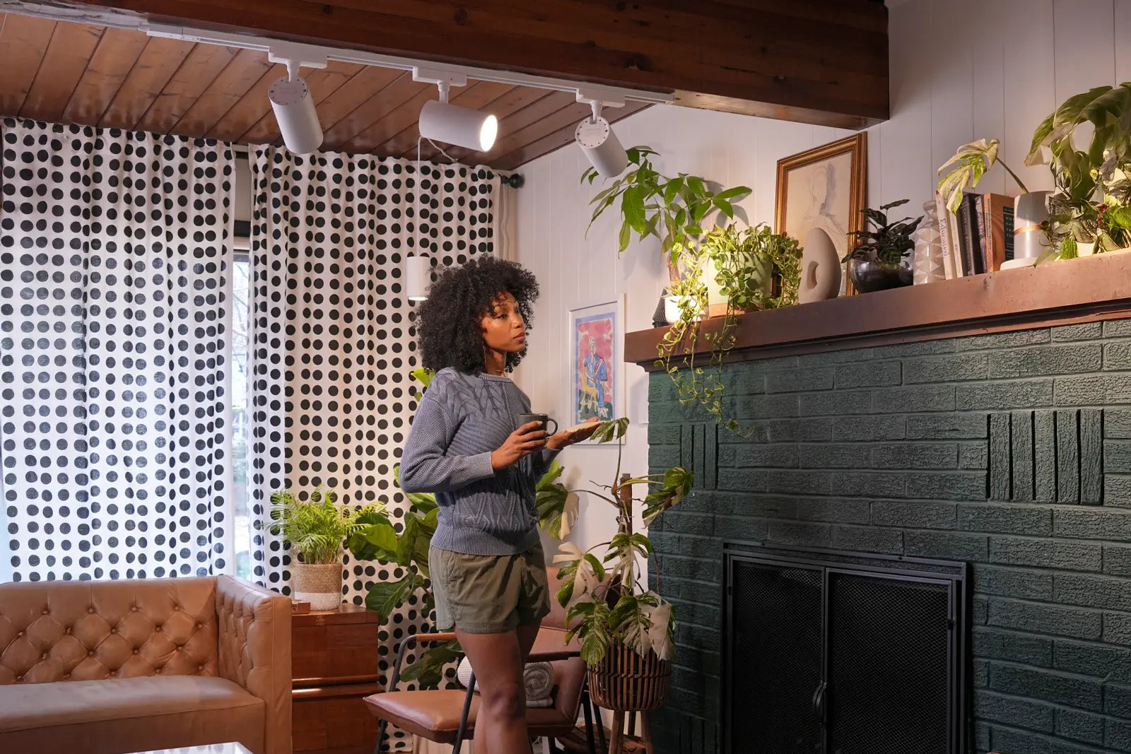 Woman standing in a modern living room with a green fireplace and decorative plants.