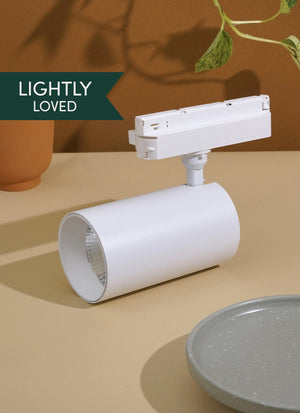 White Soltech Highland light fixture on a beige surface with a plant and pot in the background. Label that says Lightly Loved"
