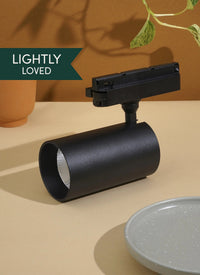 Black Soltech Highland light fixture on a beige surface with a plant and pot in the background. Label that says Lightly Loved"