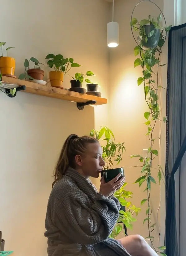 Woman sitting in a cozy room with plants and a light fixture.